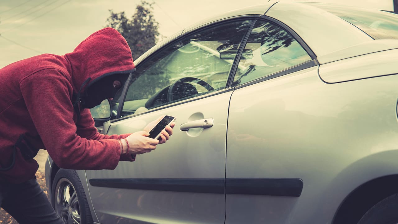 A thief using a phone to breach a car